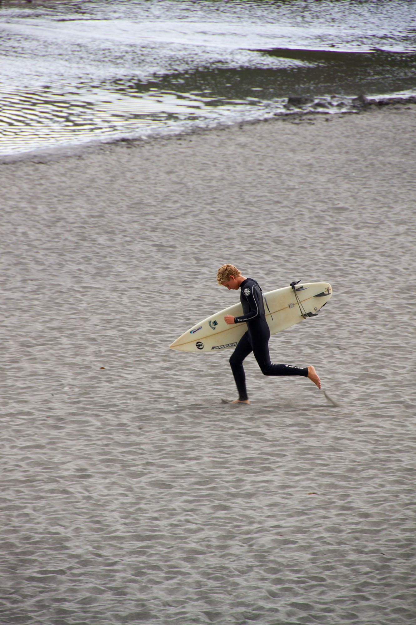 Photo of younger Surfer running at beach with surfboard in Asturias